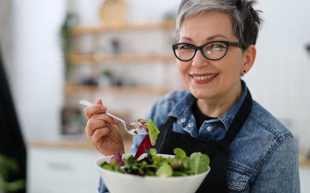 Adult smiling woman holding a plate with fresh salad, diet lunch.
